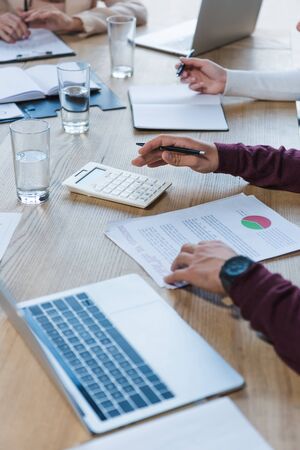 cropped view of businesspeople sitting at desk near laptops, documents and glasses of water in meeting roomの写真素材