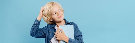 panoramic shot of smiling and dreamy kid holding books isolated on blue