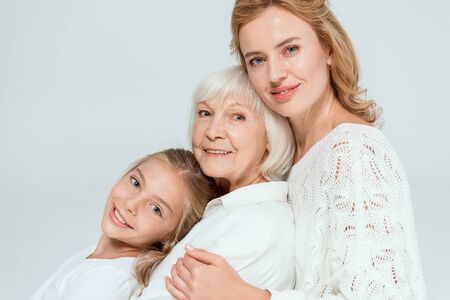 smiling granddaughter, mother and grandmother hugging isolated on greyの写真素材