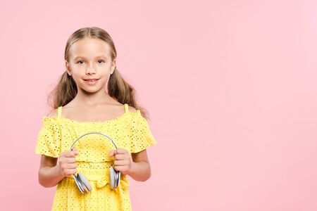 smiling and cute kid holding headphones isolated on pink