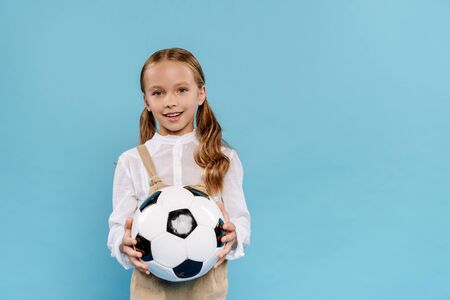 smiling and cute kid looking at camera and holding football isolated on blueの写真素材