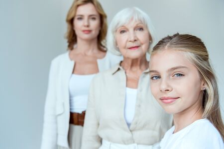selective focus of smiling granddaughter and grandmother, mother on background isolated on grey