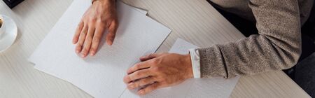 Cropped view of blind man reading braille font at table, panoramic shotの写真素材