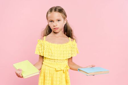 kid holding books and looking at camera isolated on pink