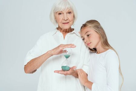 granddaughter hugging grandmother with hourglass isolated on grey
