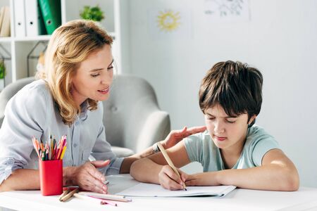 kid with dyslexia drawing with pencil and child psychologist looking at itの写真素材