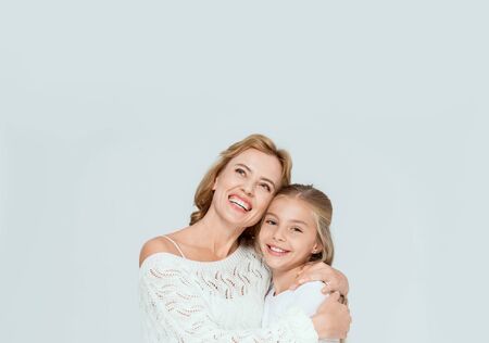 attractive mother hugging smiling daughter and looking up isolated on grey