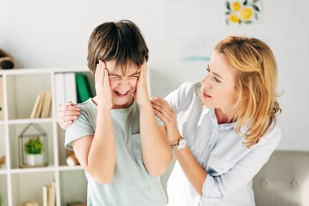 irritated kid with dyslexia and child psychologist calming him downの写真素材