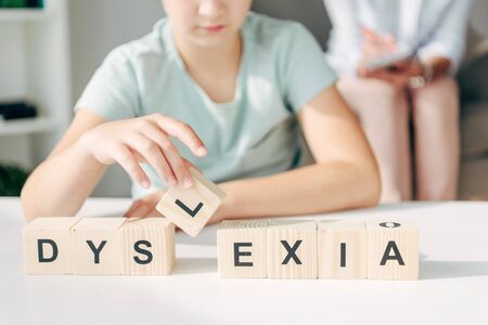 cropped view of kid with dyslexia sitting at table and playing with wooden cubesの写真素材