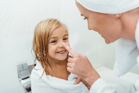 selective focus of mother touching nose of happy daughter in bathroomの写真素材