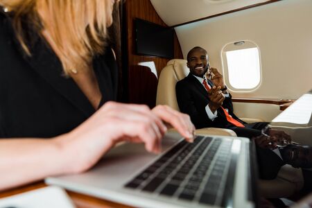 selective focus of african american businessman gesturing near businesswoman using laptop in private...