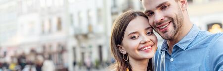panoramic shot of smiling couple of tourists taking selfie on street