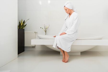 beautiful woman in white bathrobe sitting in modern bathroom