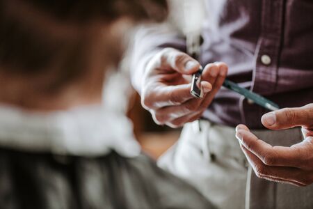 cropped view of barber holding metallic razor near man in barbershop の写真素材