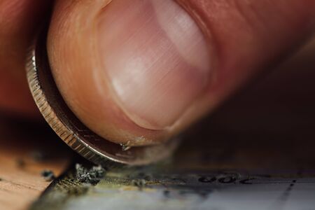 close up view of silver coin and finger of gambler scratching lottery ticket