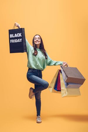 beautiful woman jumping with shopping bags on black friday, on yellowの写真素材