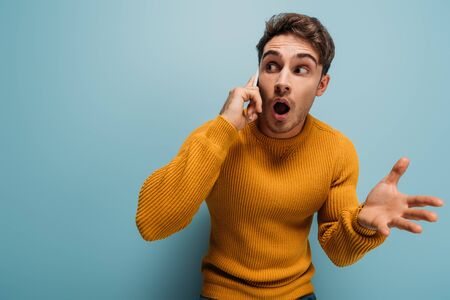 shocked handsome man talking on smartphone, isolated on blue