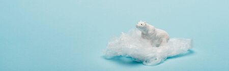 Panoramic shot of Toy polar bear on plastic packet on blue background, environmental pollution...