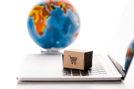selective focus of toy box on laptop keyboard near globe isolated on white, e-commerce concept