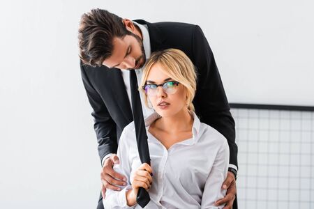 Sexy businesswoman pulling tie of businessman in officeの写真素材