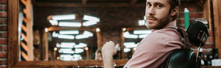 panoramic shot of handsome and bearded barber looking at camera