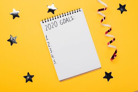 notebook with 2020 goals inscription with empty numbered points near decorative, shiny stars and serpentine on yellow surfaceの写真素材