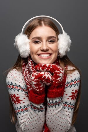 beautiful smiling woman in christmas sweater, scarf, mittens and earmuffs, isolated on greyの写真素材