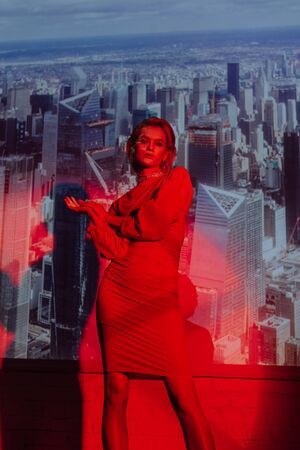 attractive and stylish woman in red dress on city background