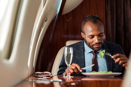 handsome african american businessman eating salad in private jetの写真素材