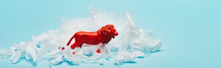 Panoramic shot of red toy lion with plastic garbage on blue background, animal welfare conceptの写真素材