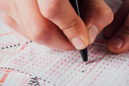 close up view of hand of gambler marking numbers in lottery ticket with pen