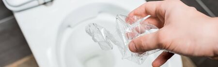 cropped view of man throwing crumpled plastic bottle in toilet bowl in modern restroom with grey...