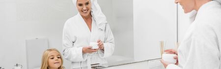 panoramic shot of happy mother holding container with cosmetic cream near cute daughterの写真素材