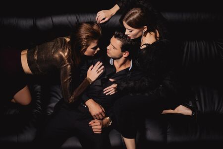 top view of attractive women kissing and hugging handsome man on black background