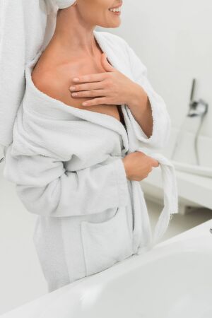 cropped view of cheerful woman in bathrobe touching body in bathroomの写真素材