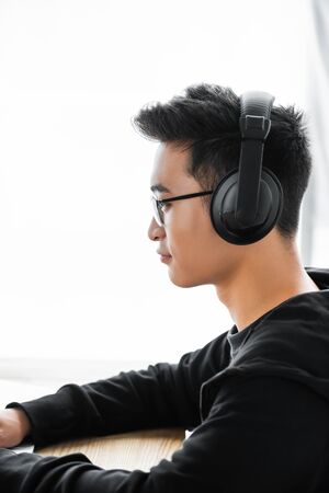 side view of asian hacker in headphones sitting at table