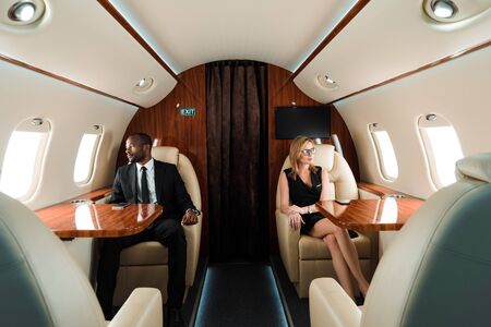 selective focus of handsome african american businessman and attractive businesswoman sitting in...