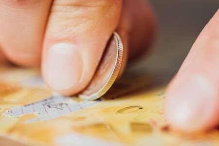 close up view of silver coin in hand of gambler scratching lottery ticket