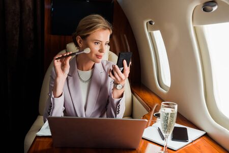 businesswoman applying decorative cosmetics near gadgets and champagne glass in private planeの写真素材
