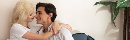 Side view of smiling couple embracing on sofa in living room, panoramic shot