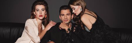 panoramic shot of attractive and stylish women hugging handsome man isolated on blackの写真素材