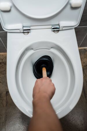 cropped view of plumber using plunger in toilet bowl in modern restroom with grey tileの写真素材