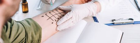 panoramic shot of allergist holding syringe near man with marked hand