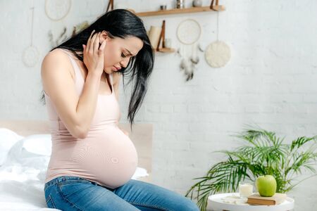 worried pregnant woman having pain and looking at belly in bedroom