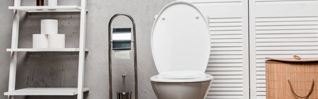interior of modern bathroom with toilet bowl near rack with towels, toilet paper, laundry basket and toilet brush, panoramic shotの写真素材