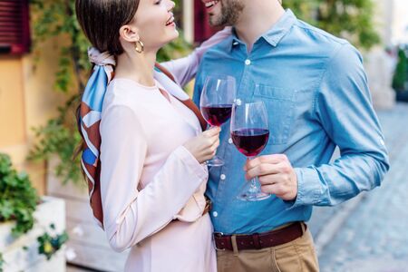 cropped view of happy couple looking at each other while holding glasses of red wine