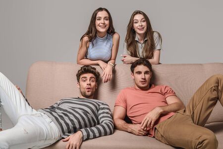 happy young friends sitting on sofa isolated on greyの写真素材