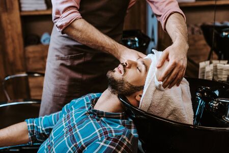 barber holding white towel near head of bearded man with closed eyes の写真素材