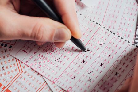 selective focus of hand of gambler marking numbers in lottery tcket with penの写真素材