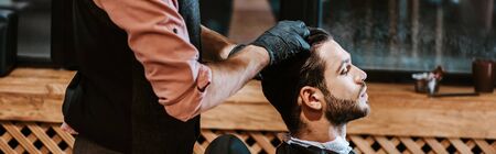 panoramic shot of barber in black latex gloves styling hair of man